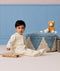 Toddler sitting on the floor in a cream patterned Sleep Onesie, playing with a wooden xylophone next to a blue pouf and plush cat.