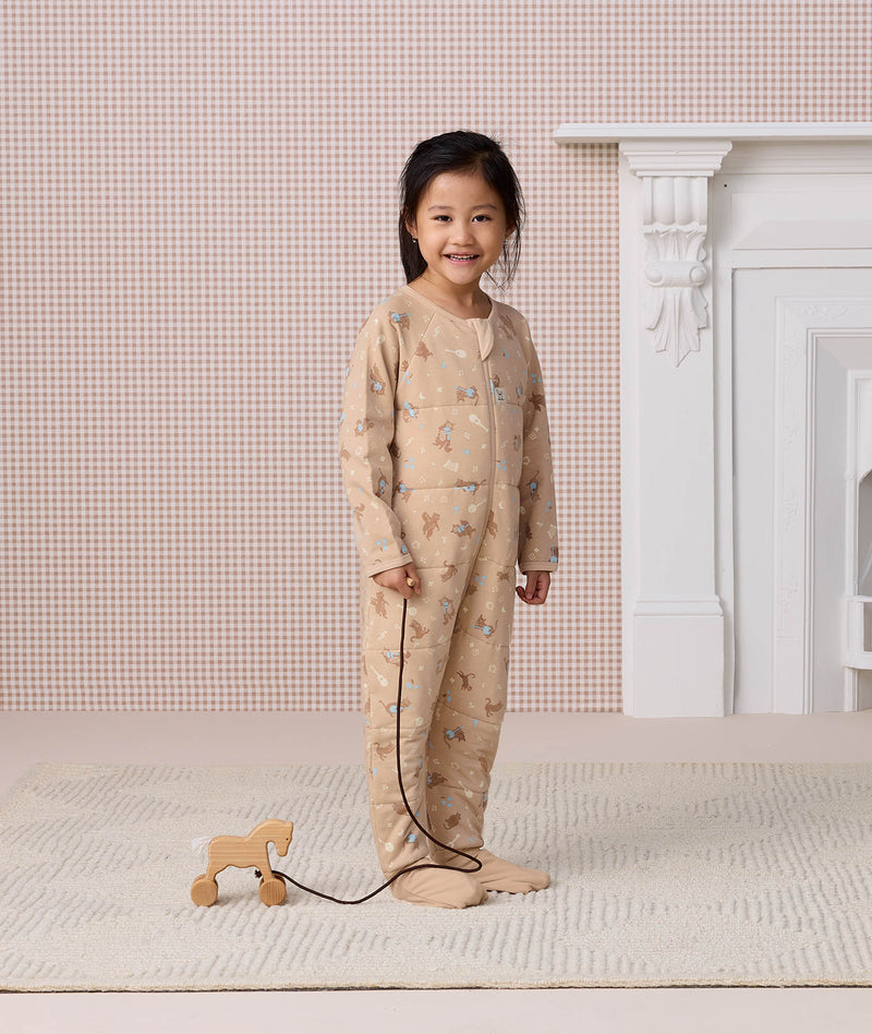 Preschooler wearing a beige patterned 2.5 TOG Sleep Onesie, standing while holding the string of a small wooden pull-along horse toy.