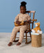 Preschooler sitting in a wooden rocking chair playing a ukulele, wearing a beige patterned Sleep Onesie with cuffed ankles.