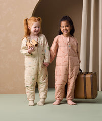 Two preschoolers are holding each other's hands, both wearing ergoPouch Sleep Onesie 2.5 TOG in Savannah and Elephant Parade colourways.