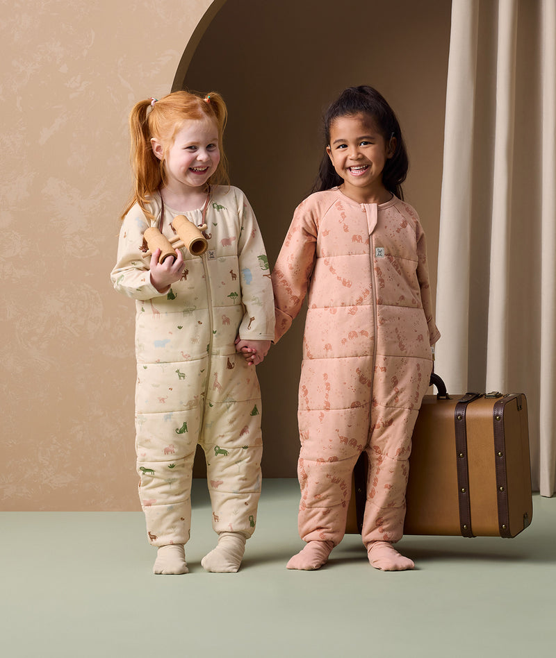 Two preschoolers are holding each other's hands, both wearing ergoPouch Sleep Onesie 2.5 TOG in Savannah and Elephant Parade colourways.