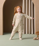 A preschooler stands and smiles while wearing an ergoPouch Sleep Onesie decorated with playful animal prints. The onesie features long sleeves, a front zipper, and foot cuffs for added comfort and flexibility, allowing for easy movement during both playtime and rest.