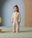 A smiling toddler stands in an ergoPouch Sleep Onesie decorated with playful animal prints. The onesie features long sleeves, a front zipper, and footed cuffs, designed to provide cozy warmth and unrestricted movement for sleep or play.
