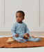 Baby sitting, wearing an ergoPouch Sleep Onesie 3.5 TOG Dragonflies