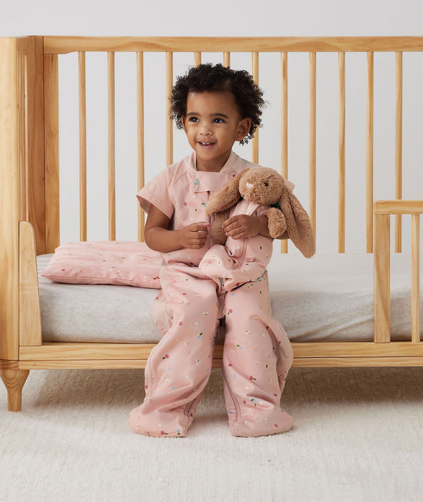 Toddler sitting on bed complete with an ergoPouch Organic Toddler Pillow Case and Sleep Suit Sack in Daisies 