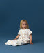 Toddler sitting in an ergoPouch Sleep Suit Bag 1.0 TOG Daydream, a sleeping bag that converts to a sleep suit with legs by a four-way zipper feature. 