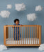 Child standing in a wooden crib wearing an ergoPouch Sleep Suit Bag 1.0 TOG Starbeam, a sleeping bag that converts to a sleep suit with legs.