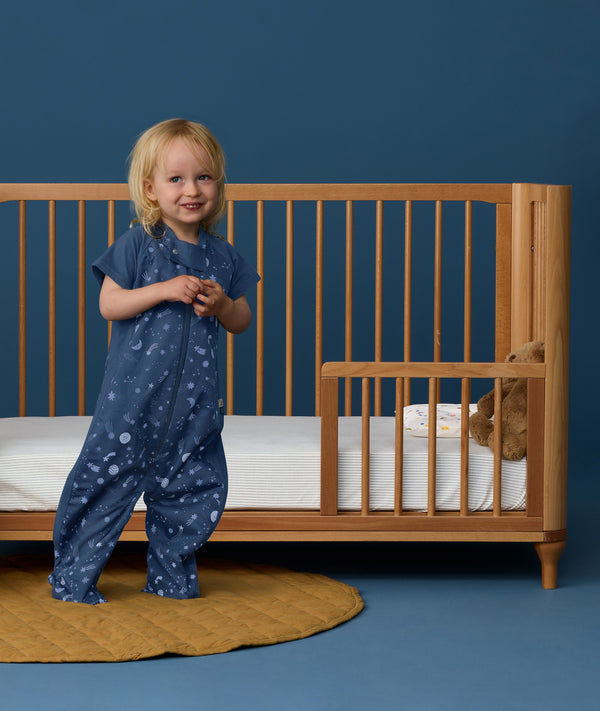 Toddler wearing an ergoPouch Sleep Suit Bag 1.0 TOG Starbeam, a sleeping bag that converts to a sleep suit with legs.