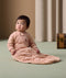 Baby sitting upright on a soft green floor, wearing a peach-colored padded sleep suit bag with a front zipper and subtle animal print.
