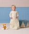 Toddler wearing a cream patterned sleep suit bag, standing in a room near a plush cat toy and a blue pouf.