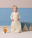 Toddler wearing a cream patterned sleep suit bag, standing in a room near a plush cat toy and a blue pouf.