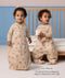 Toddler demonstrating a convertible beige Sleep Suit bag in front of a cot, with one zipped into a bag and the other split into legs. Text overlay reads: 