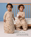 Toddler demonstrating a convertible beige Sleep Suit bag in front of a cot, with one zipped into a bag and the other split into legs. Text overlay reads: 