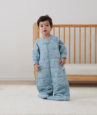 Toddler wearing a sleeved ergoPouch sleep suit bag in blue, made from organic, non-toxic materials.