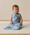 Infant sitting on a white mat, wearing an ergoPouch Sleeping Bag 0.2 TOG dragonflies