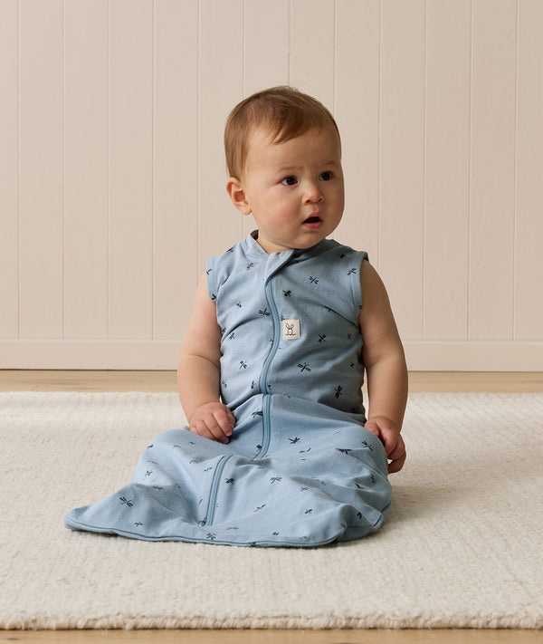 Infant sitting on a white mat, wearing an ergoPouch Sleeping Bag 0.2 TOG dragonflies