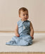 Infant sitting on a white mat, wearing an ergoPouch Sleeping Bag 0.2 TOG dragonflies