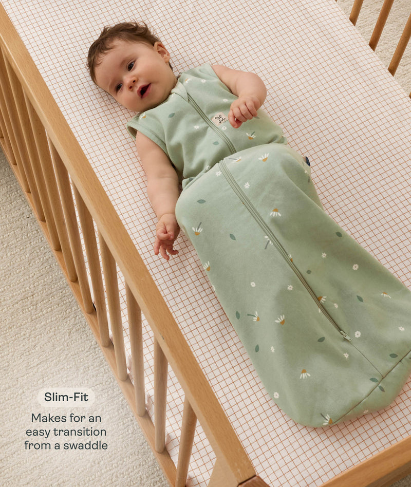 Infant dressed in a sleeveless ergoPouch Sleeping Bag 1.0 TOG, lying in a wooden cot with text highlighting 