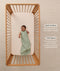 A happy baby dressed in a sleeveless ergoPouch Sleeping Bag 1.0 TOG, lying in a wooden cot with text highlighting 