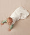 Baby crawling on a plain surface while wearing an oatmeal-coloured sleeping bag over a green long sleeved layer.