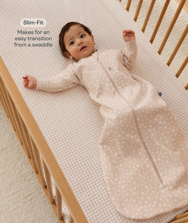 Infant lying on a grid-patterned sheet, wearing a long sleeve Sleeping Bag 1.0 TOG with text highlighting slim-fit design for easy transition from swaddling.