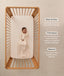 An overhead view on an infant lying in a wooden cot with a grid-patterned sheet, wearing a long sleeve Sleeping Bag 1.0 TOG with text highlighting 