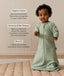 An infant wearing a long-sleeved sage green floral Sleeping Bag 1.0 TOG, standing on a padded beige mat with text highlighting 