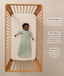 Infant lying inside a wooden cot, wearing a long-sleeve Sleeping Bag 1.0 TOG with text highlighting 