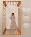A happy baby lying in a wooden cot, wearing a sleeved Sleeping Bag 1.0 TOG Taupe Marle with text highlighting 