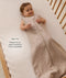 Infant lying in a wooden cot, wearing an ergoPouch Sleeping Bag  1.0 TOG Taupe Marle with text highlighting 