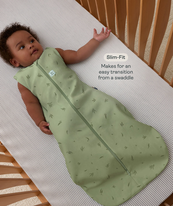 Infant lying in a wooden cot wearing a sleeveless Sleeping Bag 1.0 TOG Willow with text highlighting slim-fit design for an easy transition from swaddling.