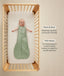 Baby lying on their back inside a wooden cot wearing a green sleeveless Sleeping Bag 1.0 TOG with text callouts highlighting wash & wear care and TOG rating features.