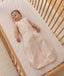 Infant wearing a beige patterned sleeveless Sleeping Bag 1.0 TOG, lying inside a wooden cot with a grid-patterned sheet