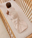 An overhead view of a baby wearing a pattern-printed sleeveless Sleeping Bag, crawling on their hands and knees inside a wooden cot with a grid sheet.