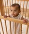 A baby wearing a printed sleeveless Sleeping Bag, standing and holding onto the rail of a wooden cot.