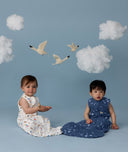 Two children sitting wearing an ergoPouch Sleeping Bag 1.0 TOG Daydream and Starbeam, on a blue background with clouds and birds.