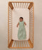 An overhead shot of an infant lying in a wooden cot, wearing a sleeveless floral-patterned Sleeping Bag 1.0 TOG