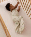 An infant wearing a cream safari-themed 1.0 TOG Sleeping Bag lying on its side in a wooden cot.