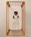 A happy baby lying inside a wooden cot, wearing a sleeveless, safari-themed Sleeping Bag.