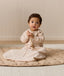 Infant sitting on a quilted mat while holding a wooden toy, wearing a long-sleeve patterned Sleeping Bag 1.0 TOG