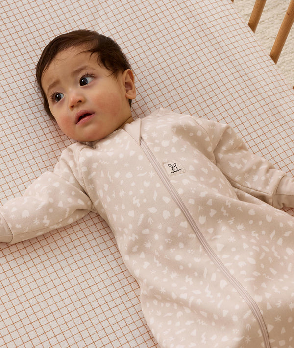 Infant lying on a grid-patterned sheet, wearing a long sleeve Sleeping Bag 1.0 TOG featuring front zipper.