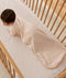 An overhead view of a baby wearing a pattern-printed long-sleeved Sleeping Bag, crawling on their hands and knees inside a wooden cot with a grid sheet.