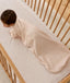An overhead view of a baby wearing a pattern-printed long-sleeved Sleeping Bag, crawling on their hands and knees inside a wooden cot with a grid sheet.