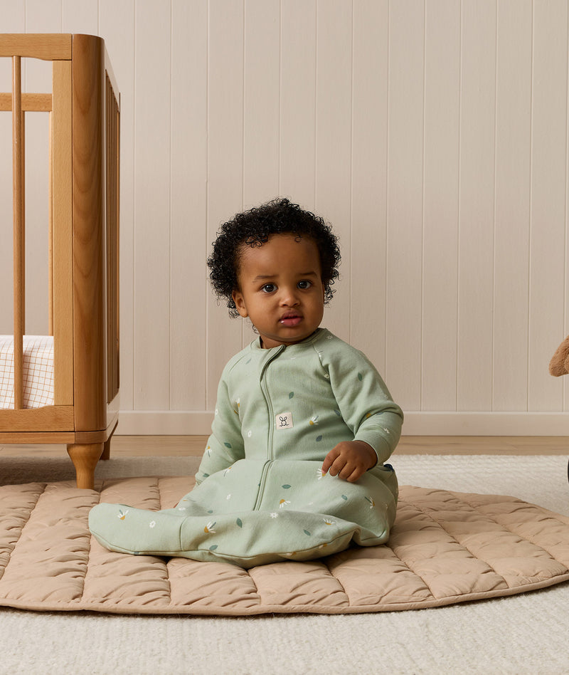 Infant sitting upright on a quilted mat, wearing an ergoPouch Sleeping Bag 1.0 TOG Sleeved
