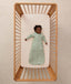 Infant lying inside a wooden cot with a grid-patterned sheet, wearing a long-sleeve Sleeping Bag 1.0 TOG