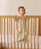 Infant standing inside a wooden cot wearing a long-sleeve 1.0 TOG Sleeping Bag with safari animal print