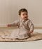 Infant wearing a long-sleeve Sleeping Bag 1.0 TOG Taupe Marle, sitting on a quilted mat