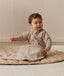 Infant wearing a long-sleeve Sleeping Bag 1.0 TOG Taupe Marle, sitting on a quilted mat