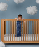 Child standing in a wooden crib wearing an ergoPouch Sleeping Bag 1.0 TOG Starbeam