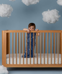 Child standing in a wooden crib wearing an ergoPouch Sleeping Bag 1.0 TOG Starbeam